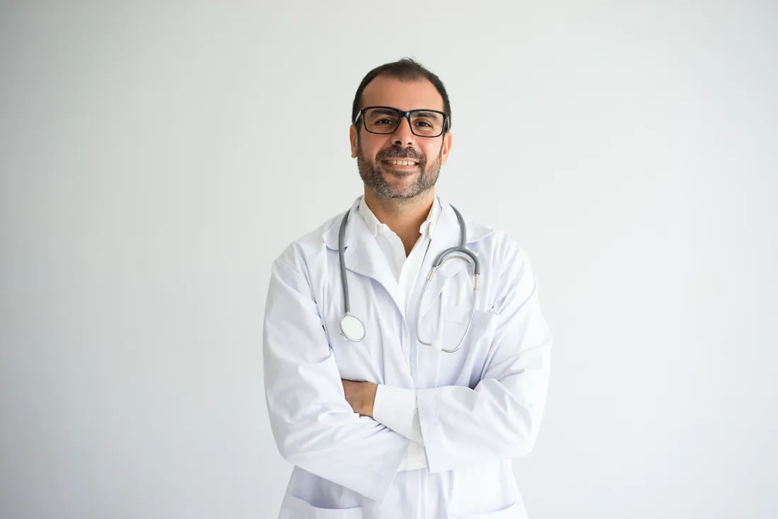 Médico de jaleco e estetoscópio, de braços cruzados, sorrindo