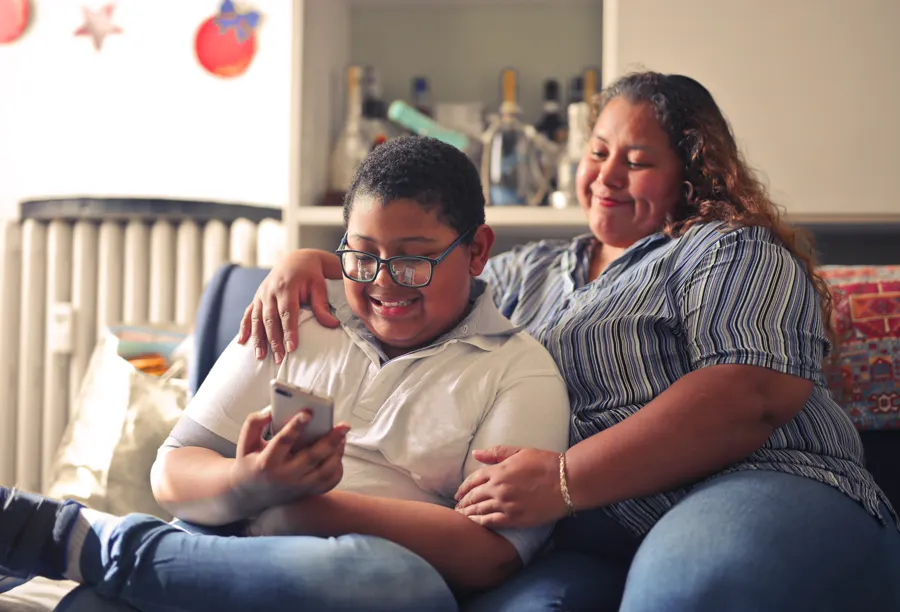 Mãe e filho no sofá de casa mandando mensagem pelo celular